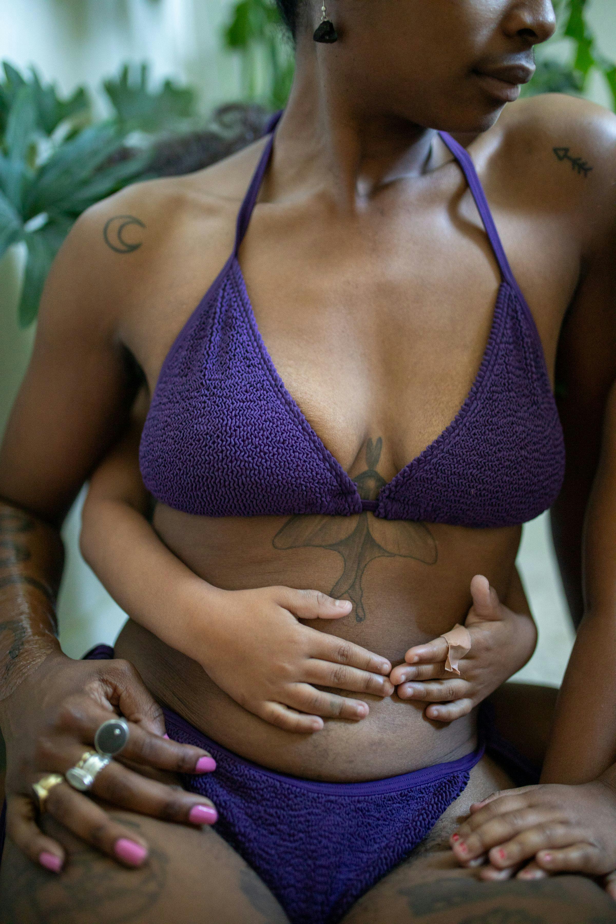 Close-up of Bri with her child, wearing Damson purple swimsuit