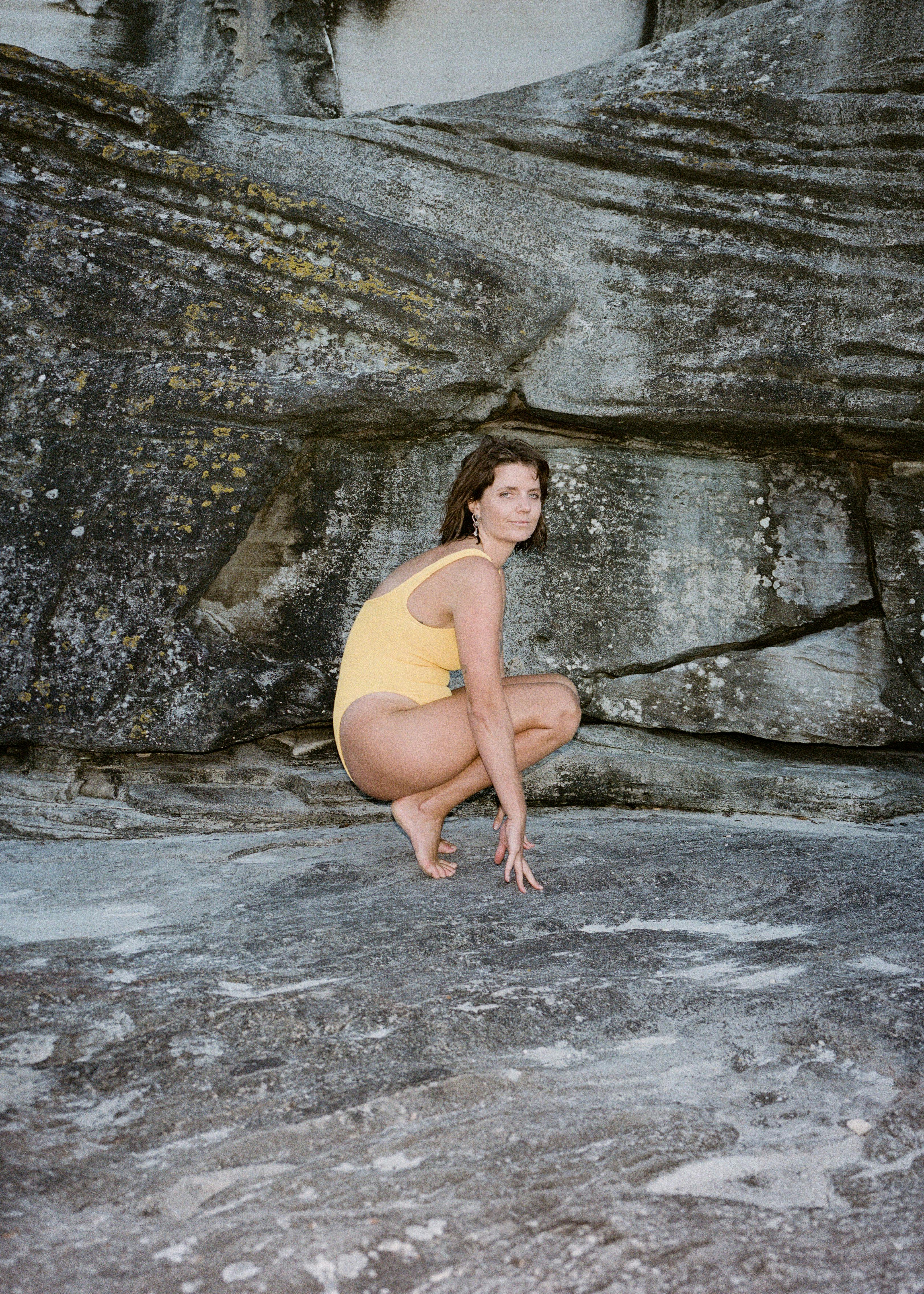 Lucy on rocks in yellow swimsuit