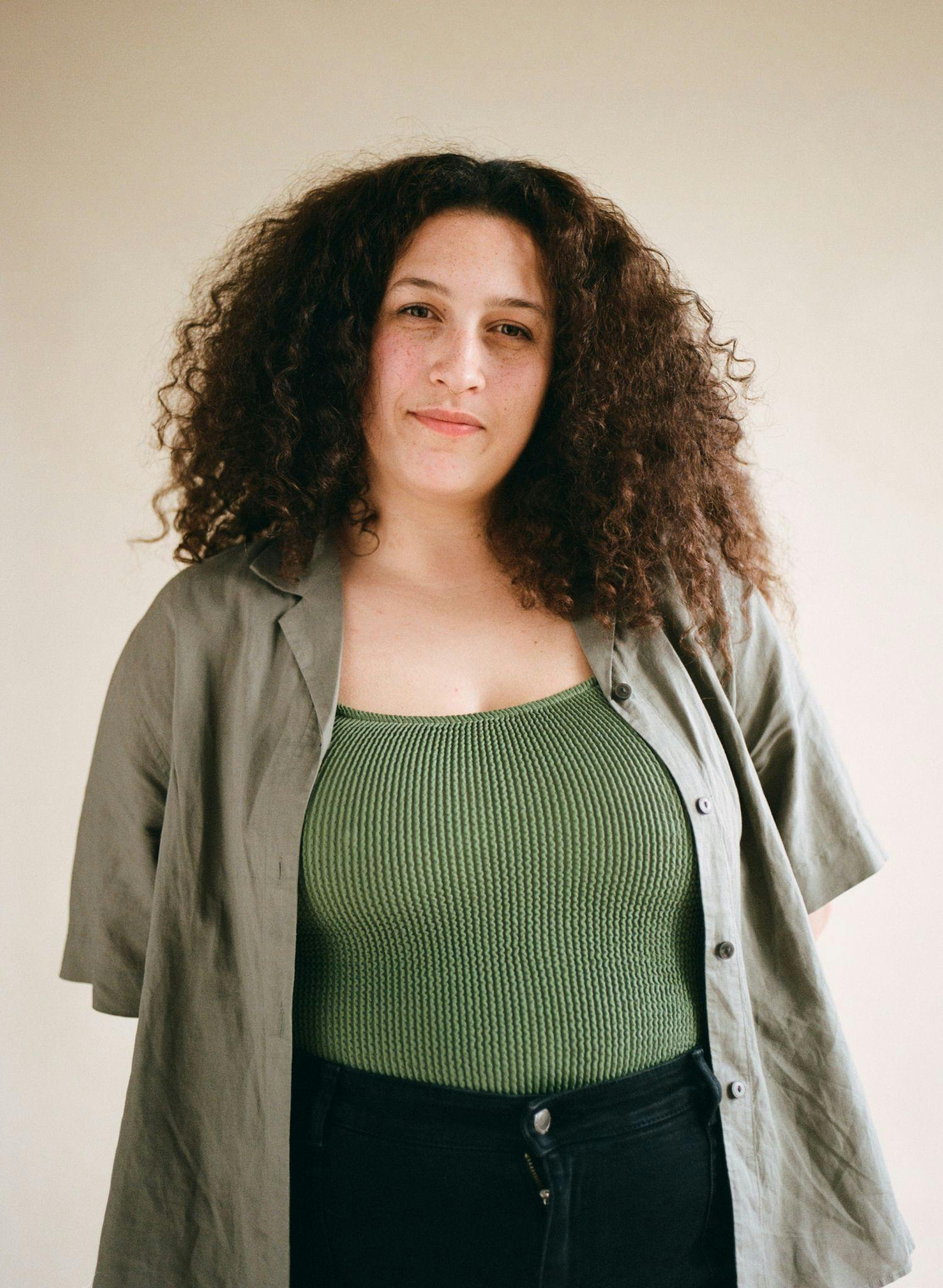 Portrait of Nanci standing in green shirt and swimsuit with black pants.